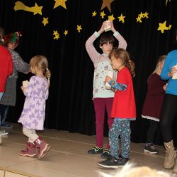 Eine Gruppe von Kindern mit Kerzen in der Hand laufen auf einer Bühne um ein anderes Kind mit Kerze in der Hand herum.