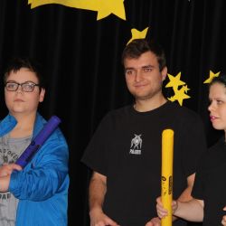 3 Schüler*inen stehen auf der Bühne mit Musik Rohren in der Hand.