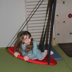 Ein Kind auf einer Indoor Schaukel, im Hintergrund eine Kletterwand.