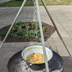 Ein Schwenktopf über einer Feuerschalle in dem eine Suppe gekocht wird.