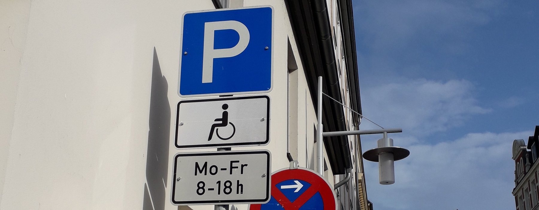 Ein Foto von einem Straßen Schild, welches das Parken Symbol Zeigt da drunter Behindertenparkplätze und die Zeiten Mo-Fr 08-18 Uhr.