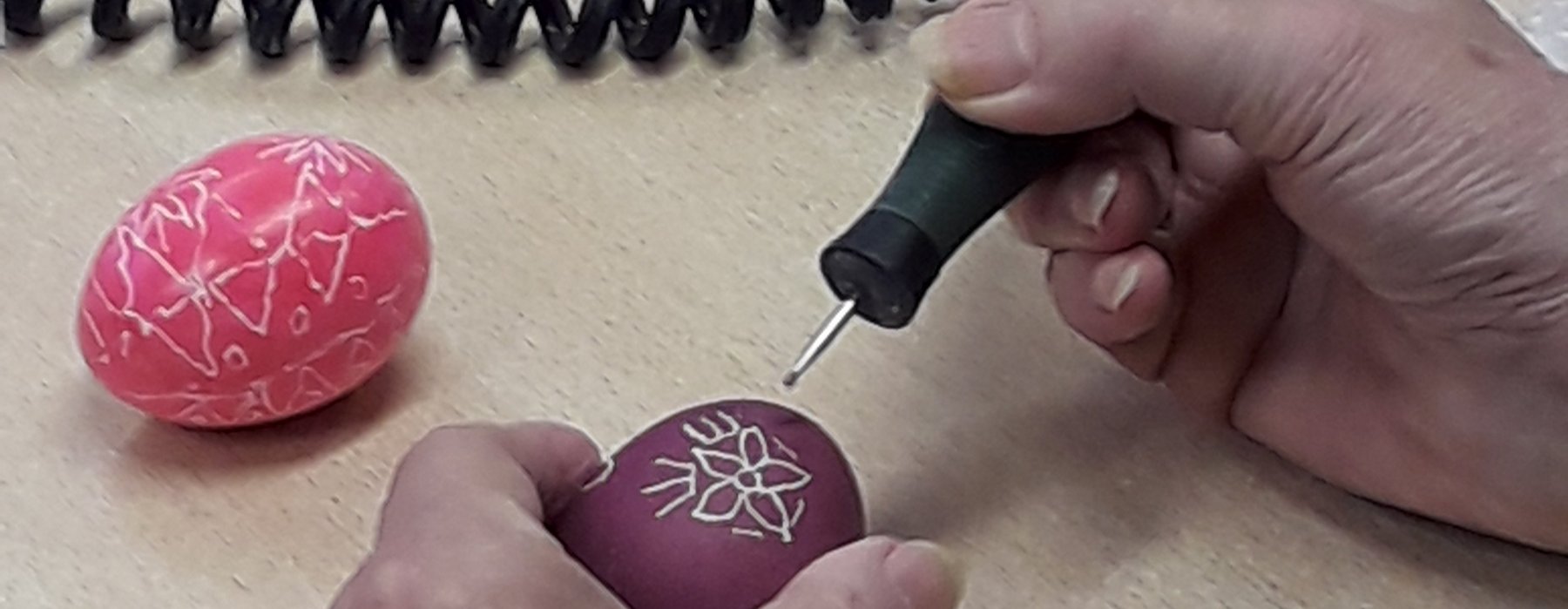 Eine Person graviert vor bemalte Eier in verschieden Mustern.